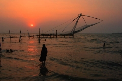 A local woman enjoys the sunset alongside Chinese fishing nets in Kerala, India