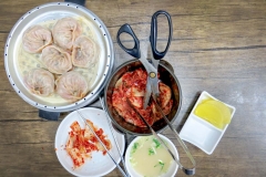 A typical assortment of Korean food - kimchee, dumplings, soup and scissors to cut it all up