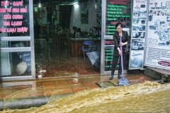 A shopkeeper tries using a broom to keep monsoon rains out of her business
