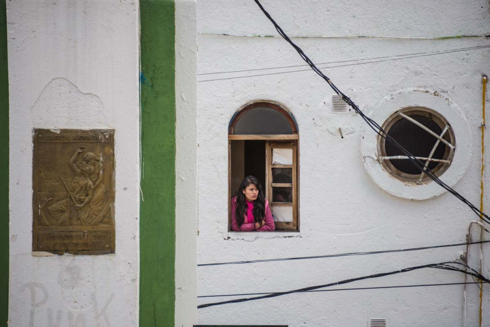 A woman watches a celebration from a window above Oruro's Plaza Folklore