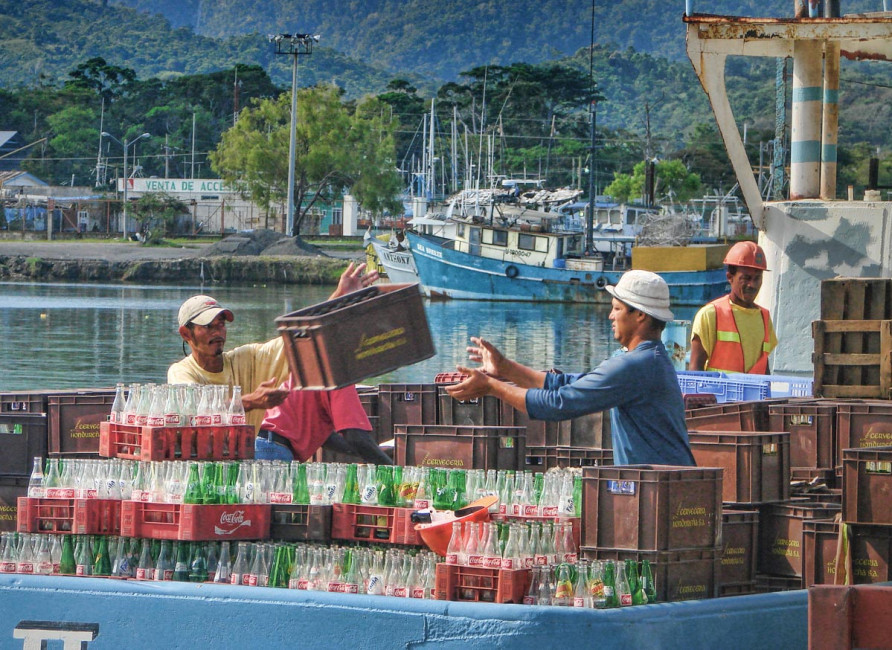 Local workers toss empty crates of soda onto a pier, after being consumed by tourists on the Bay Islands