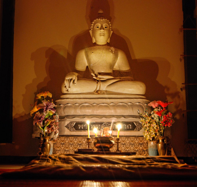 Candles illuminate a Buddha statue at Wat Umong during an evening meditation