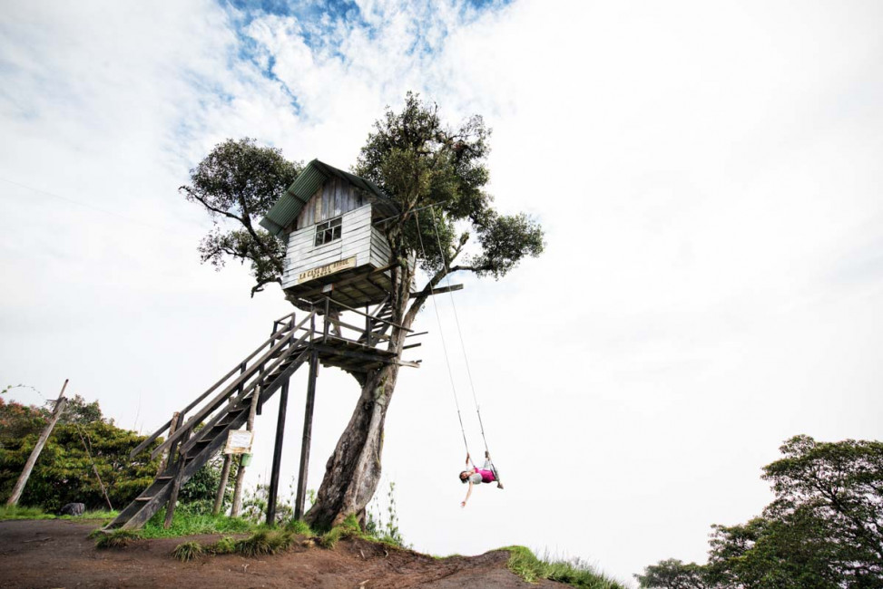 Carrie swings from a treehouse at Casa del Arbol - alongside the Tungurahua Volcano ... which is shrouded by clouds