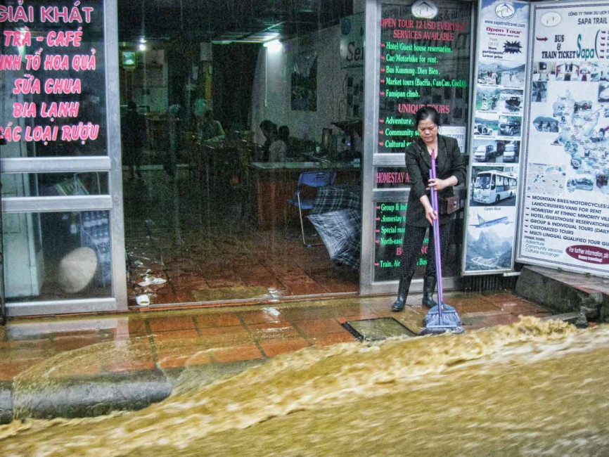A shopkeeper tries using a broom to keep monsoon rains out of her business