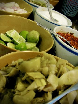Onions, limes, pickled cabbage, chili flakes, sugar, and vinegar sauce are all on the table to add flavor to your Kho So