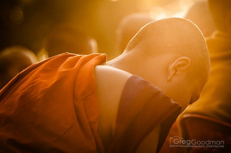 A monk bows his head in prayer as the sun rises above him