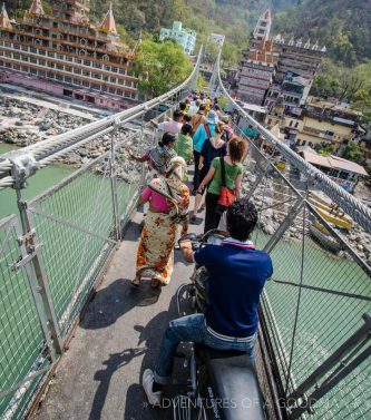 Tourists, motorcycles, locals, cows and monkeys cross the Laxshman Jhula Bridge in Rishikesh, India