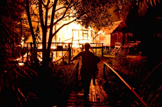 Christian escapes across a bamboo bridge after running into his burning bamboo hut to save his favorite sweatshirt