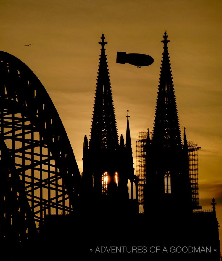 A blimp flies by the Kolner Dom at sunset